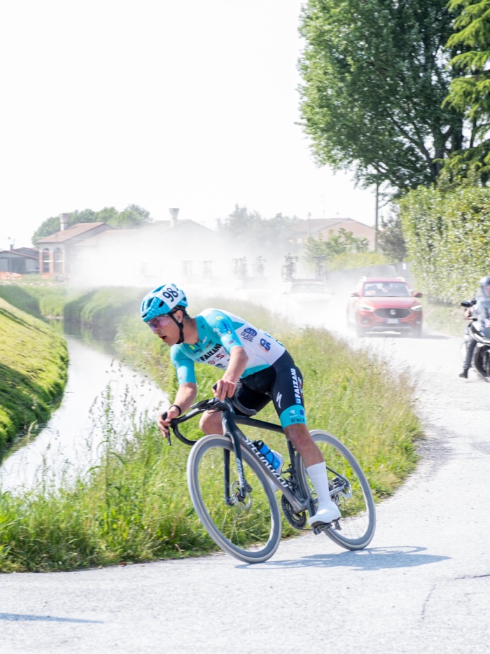 Ciclista in fuga su una strada polverosa, seguito dall'ammiraglia