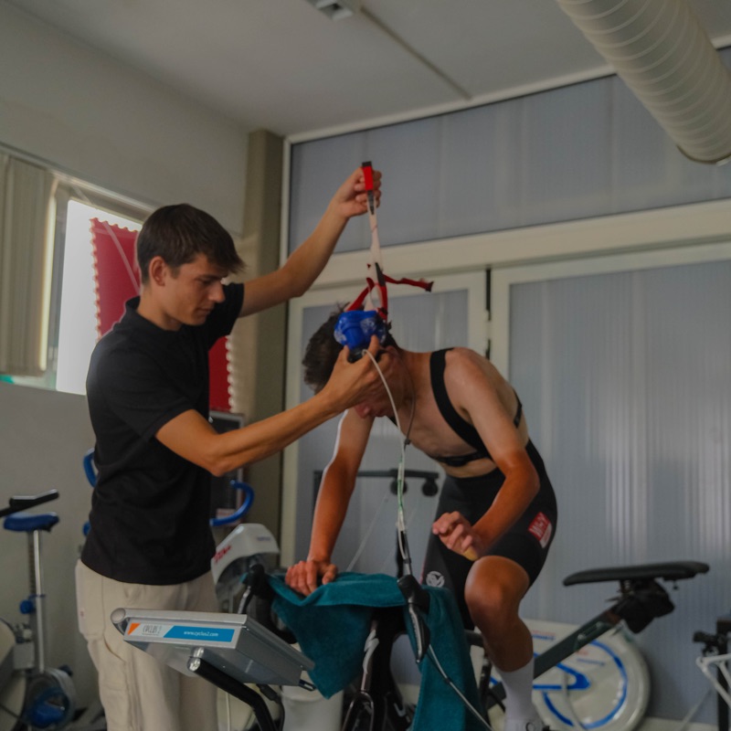 Il coach sistema la maschera dell'analizzatore sul volto dell'atleta seduto al cicloergometro