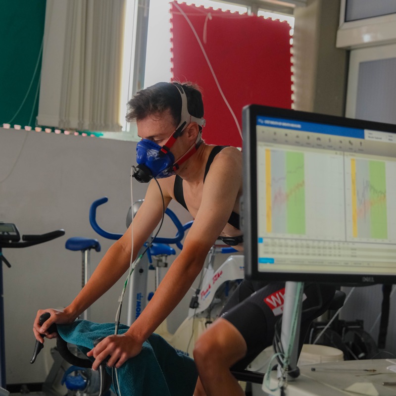 Atleta con la maschera al cicloergometro durante il protocollo incrementale, accanto al monitor con le curve del test