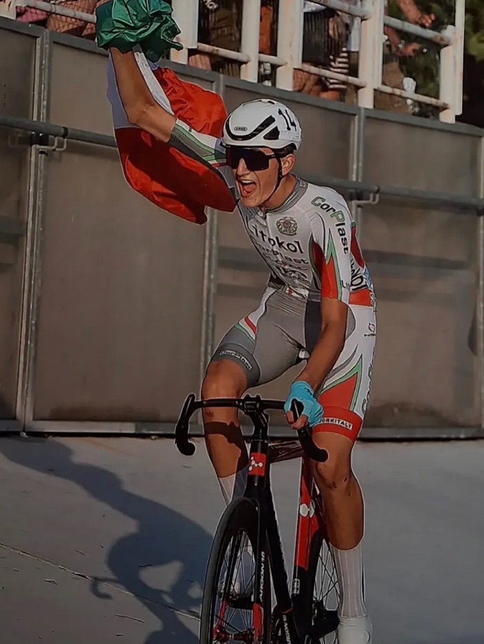 Un atleta seguito alza le braccia sul traguardo con la bandiera italiana